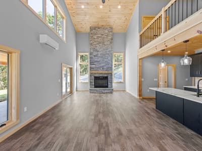 Floor-to-ceiling stacked-stone fireplace between two windows in the unfurnished great room, the kitchen island to the right