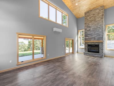 Stone fireplace with a wood mantel under clerestory windows, a mini-split on the wall and glass doors reflecting the patio
