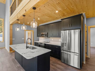 Kitchen with dark cabinets, marble-look island, glass pendants and stainless appliances beneath the pine loft beam