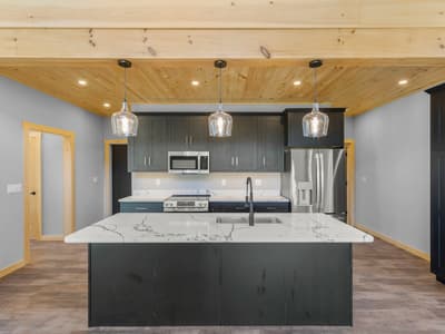 Kitchen elevation with three glass pendants over the island sink, dark cabinets, and a stainless French-door refrigerator