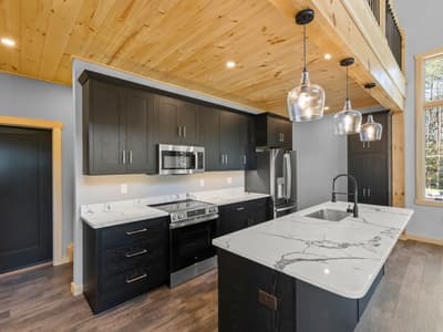 Kitchen corner with a stainless range and microwave, marble-look counters, and a window into the pines