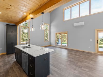 Kitchen island with sink and stainless dishwasher facing the empty great room, a mini-split high on the wall and glass door beyond