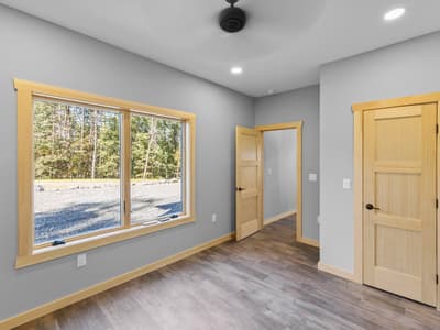 Unfurnished bedroom with a wide window facing the gravel clearing, pine doors to the hall and closet, and a ceiling fan