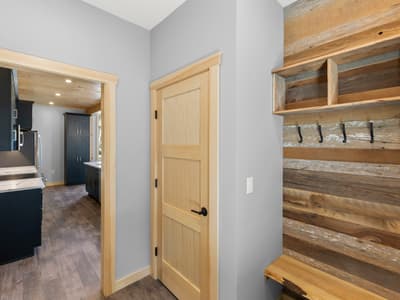 Mudroom wall of reclaimed barnwood with black coat hooks, a cubby shelf and live-edge bench, the kitchen visible through the doorway