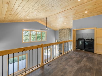 Loft with a black washer and dryer in an open alcove beside the stacked-stone chimney and a sliding pine door