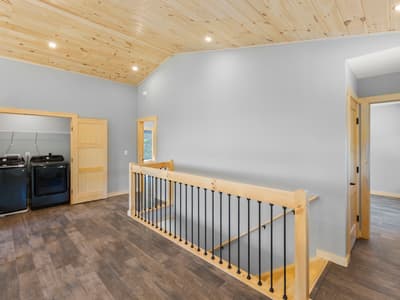 Upstairs landing with an open laundry closet holding a black washer and dryer, next to the timber stair railing