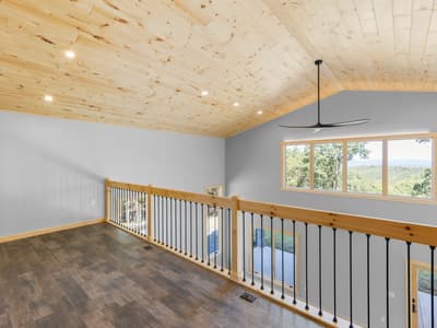 Empty loft with a picture window framing a long ridge view, a black ceiling fan and railing overlooking the great room