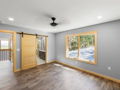 Bedroom with a sliding pine barn door open to its bathroom vanity, and a window onto the gravel drive