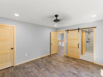 Bedroom corner with an open pine door toward the loft and a sliding barn door revealing the tiled walk-in shower