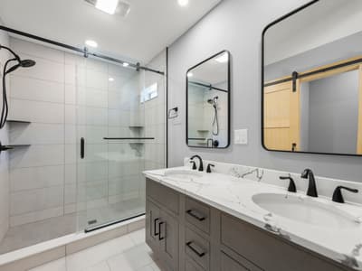 Bathroom with a dark-wood double vanity, marble-look top, two black-framed mirrors and a glass-doored tile shower