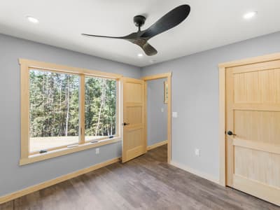 Unfurnished bedroom with a ceiling fan and a wide pine-trimmed window onto the field at the wood's edge