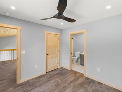 Bedroom with its own bathroom — toilet and gray vanity seen through the doorway — and the loft railing visible down the hall