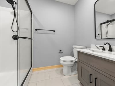 Bathroom with a glass-doored fiberglass shower, black fixtures, toilet, and gray vanity below a black-framed mirror