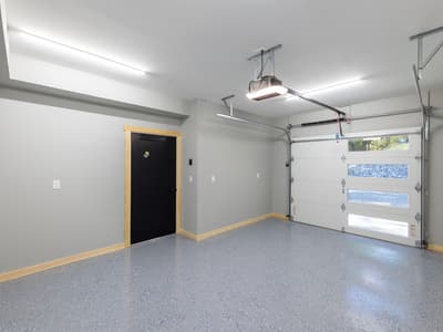 Garage interior with a speckled epoxy floor, a white insulated door with window lites onto the rock bank, and a black entry door