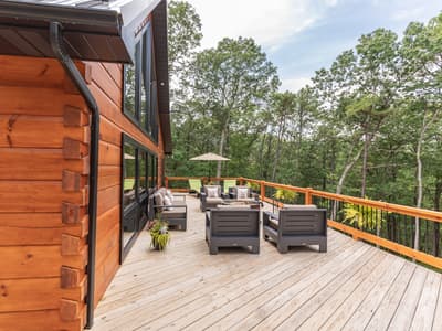 Deck corner with an outdoor sofa, loungers and a market umbrella against dense forest