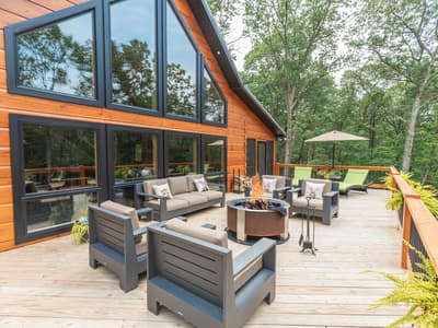 The gable window wall seen from the deck, with a lit fire pit and lounge seating in front