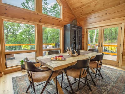 Dining area with a live-edge table beneath a vaulted ceiling and a wall of windows onto the forest