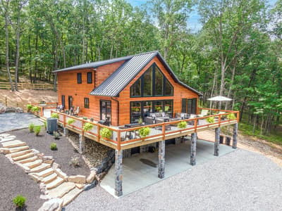 Aerial view of the log home showing its gable end, wraparound deck and metal roof against dense forest