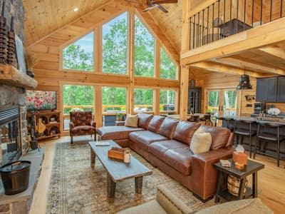 Great room with a floor-to-ceiling stone fireplace, leather sectional and a gable window wall of trees
