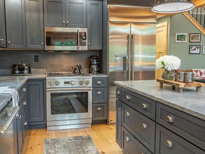 Kitchen range and stainless refrigerator in slate-blue cabinetry, a runner rug on the floor between the counters