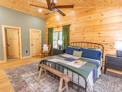 Main bedroom with a king bed, a sage accent wall and a rustic bench at its foot