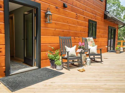 Side porch with rocking chairs and potted flowers beside an open front door