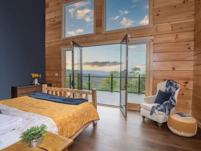 Main bedroom with a log bed and gold bedding, French doors standing open to the deck and the ridge at dusk