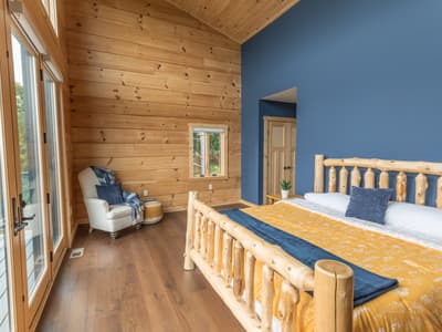 The main bedroom from the opposite corner, a navy accent wall behind the bed and doors to the deck