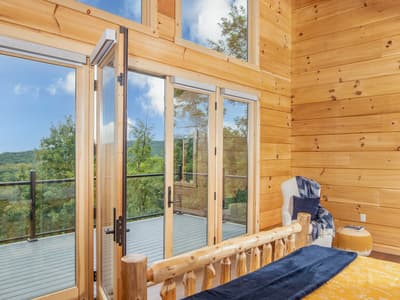 The bed and open deck doors from the foot of the bed, wood-paneled walls rising to a vaulted ceiling and one wall painted navy