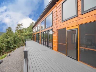 The deck running the length of the window wall, cable railing above a wooded hillside