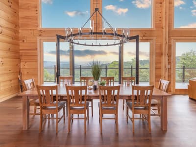 Dining table set symmetrically beneath an iron ring chandelier, the window wall looking out to the ridge