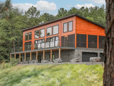 The home seen from the meadow below, log walls warm in late light above tall grass