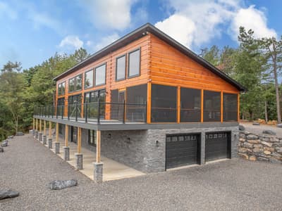 Three-quarter view from the drive, the deck carried on timber posts above a stone walkout with two garage bays