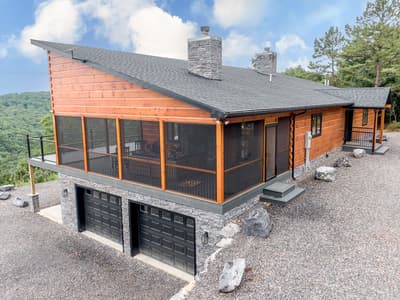 Elevated corner view showing the screened porch, two stone chimneys and garage doors set into the stone lower level