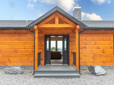Front entry beneath a timber gable portico, double doors standing open to the valley beyond