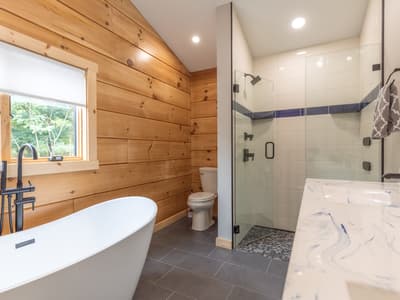 Bathroom with a freestanding tub against a wood-paneled wall, a tiled shower and a marbled vanity top