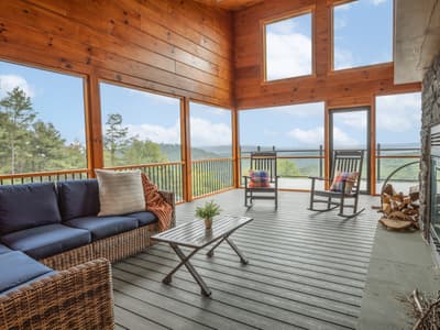 Screened porch with a wicker sectional, two rocking chairs, a stone fireplace and layered ridges beyond