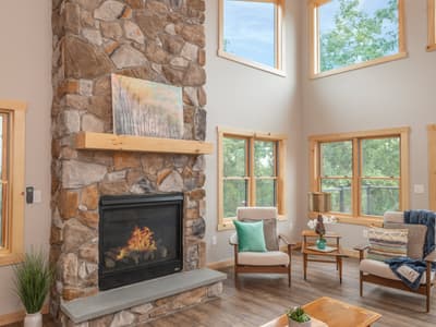 Tall stone fireplace with a lit fire and a timber mantel, beneath a vaulted pine ceiling