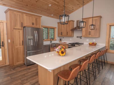Kitchen with hickory cabinets, a white quartz peninsula, lantern pendants and leather bar stools