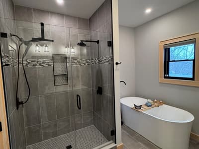 Tiled walk-in shower with a rainhead and a mosaic band, beside a freestanding tub