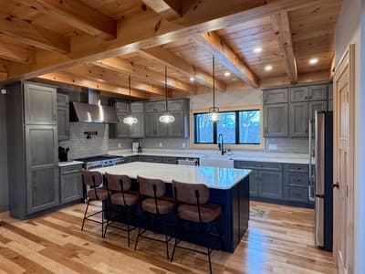 Kitchen with gray cabinets, a quartz island and leather stools, beneath an exposed beam ceiling