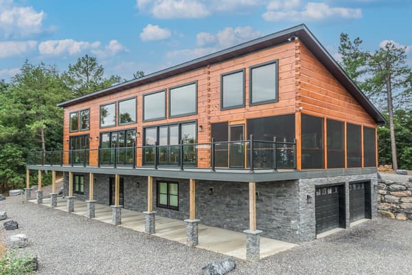 A modern log home with a long glass-railed deck above a stone lower level