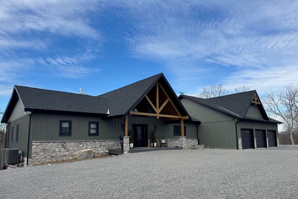 A lodge-style hybrid home with dark green siding and timber trusses