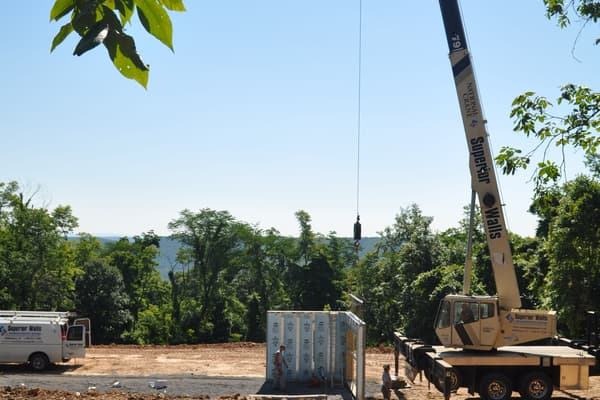 The crane boom raised against the trees, an outrigger set on the bare pad, ready to start setting panels.
