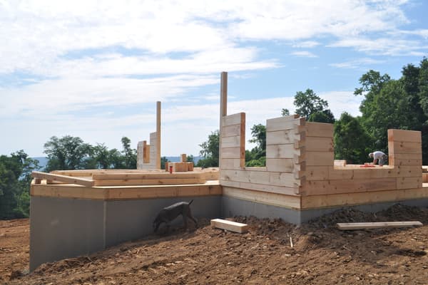 The first courses of log wall on the deck, square-cut timbers stacked two and three high, the valley in the distance.