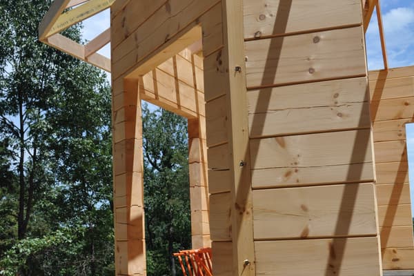 A dormer framed out against the sky, new joists and sheathing pale against the darker log wall below.