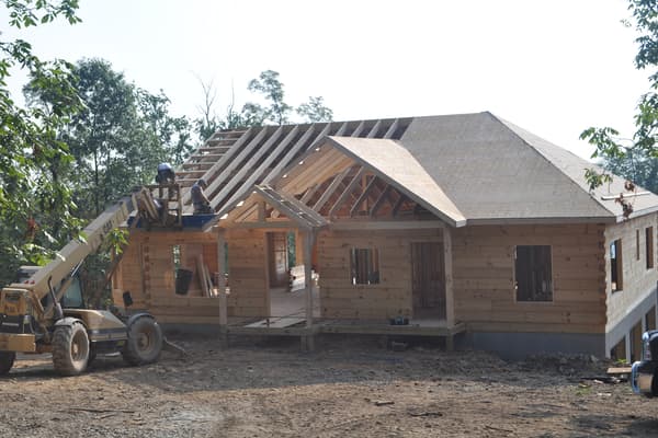 The roof going on, trusses set across the main run and a telehandler parked alongside with more material.