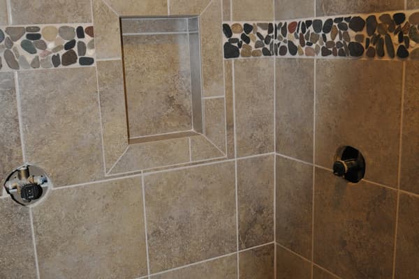 A tiled shower with a bench and an inset niche, a band of river stone across the wall.