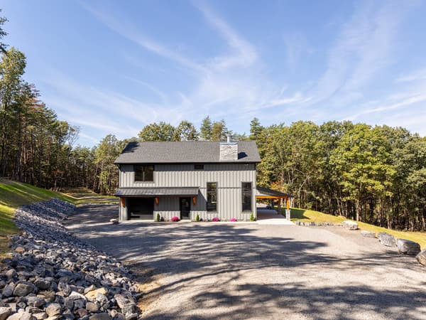 A stick-built modern farmhouse with board-and-batten siding and a stone chimney