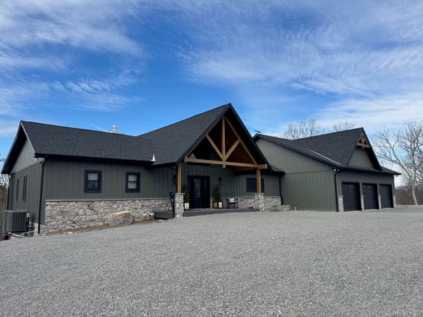 A lodge-style hybrid home with dark green siding and timber trusses